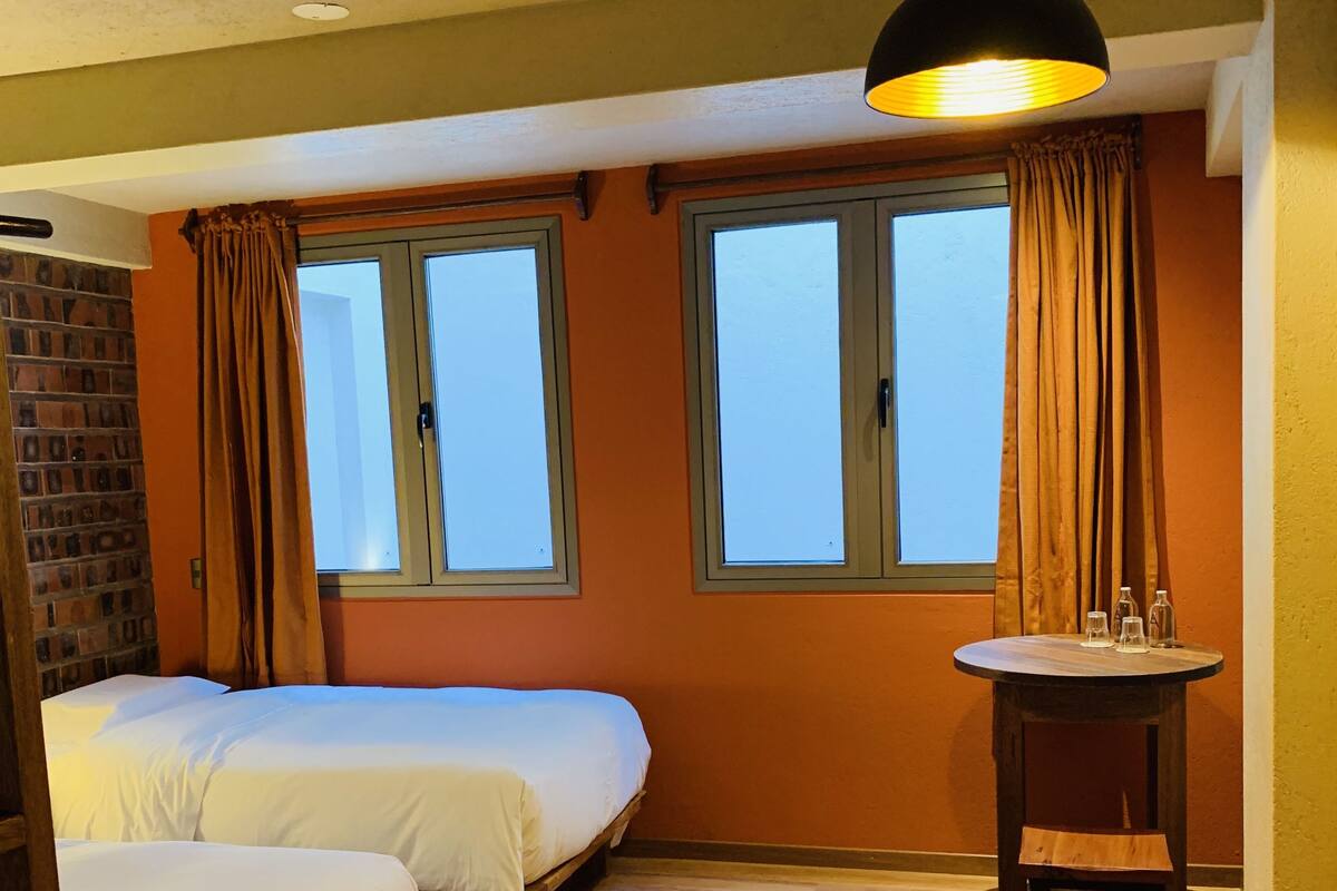A room with two beds, a table with chairs, and a window with curtains.