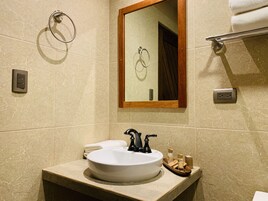 Un baño con un lavamanos blanco, un espejo con marco de madera, un perchero para toallas y un jabonera.