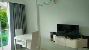 Ein modernes Zimmer mit weißem Schreibtisch, einem Stuhl, einem Flachbildfernseher auf einer weißen Kommode und einer Klimaanlage an der Wand.