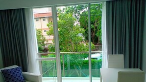 Ein modernes Wohnzimmer mit einem weißen Sofa, einem weißen Tisch und Blick auf einen Balkon mit Grünpflanzen und Gebäuden im Hintergrund.