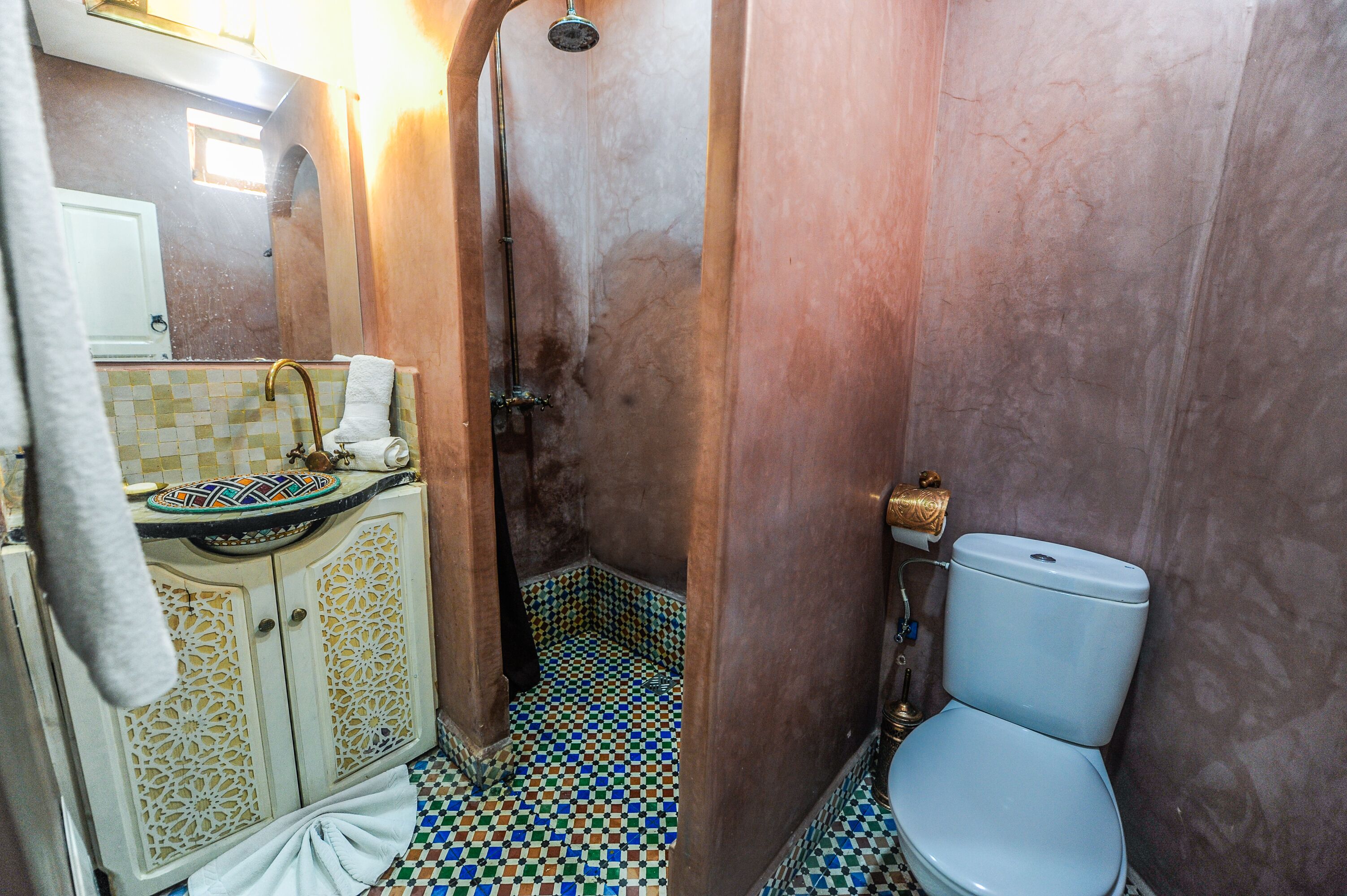 Un baño con piso de baldosas, un lavamanos con lavabo decorativo, un inodoro y una zona de ducha.
