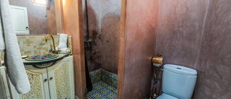 Un baño con piso de baldosas, un lavamanos con lavabo decorativo, un inodoro y una zona de ducha.