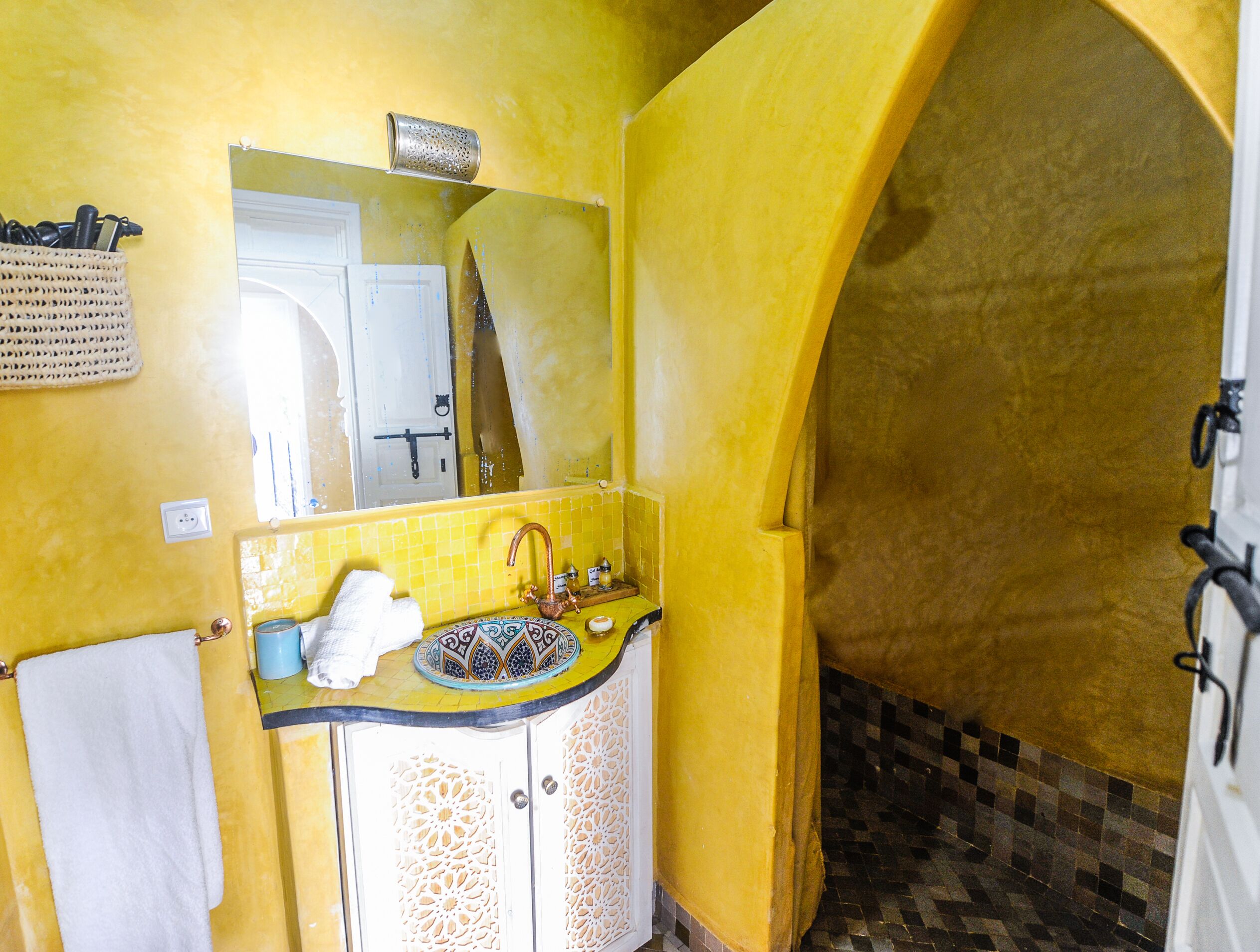 A bathroom with yellow walls, a white sink with a copper faucet, and a decorative mirror above it.