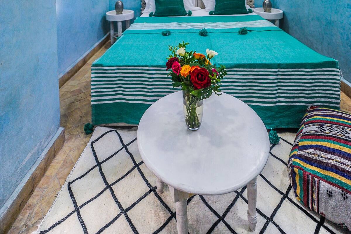 A bedroom with a large bed, a round table with a vase of flowers, and a decorative ceiling light.