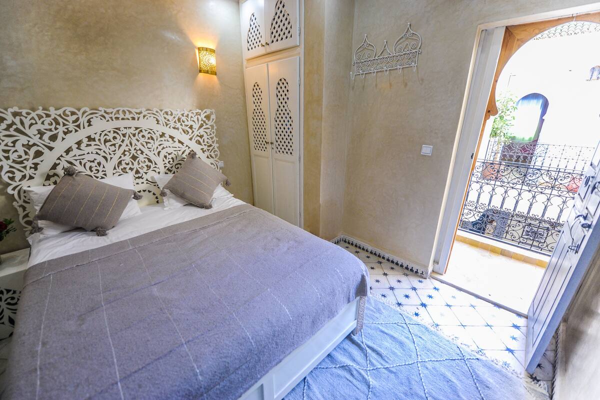 A bedroom with a bed, a decorative headboard, a wardrobe, and a balcony with a railing.