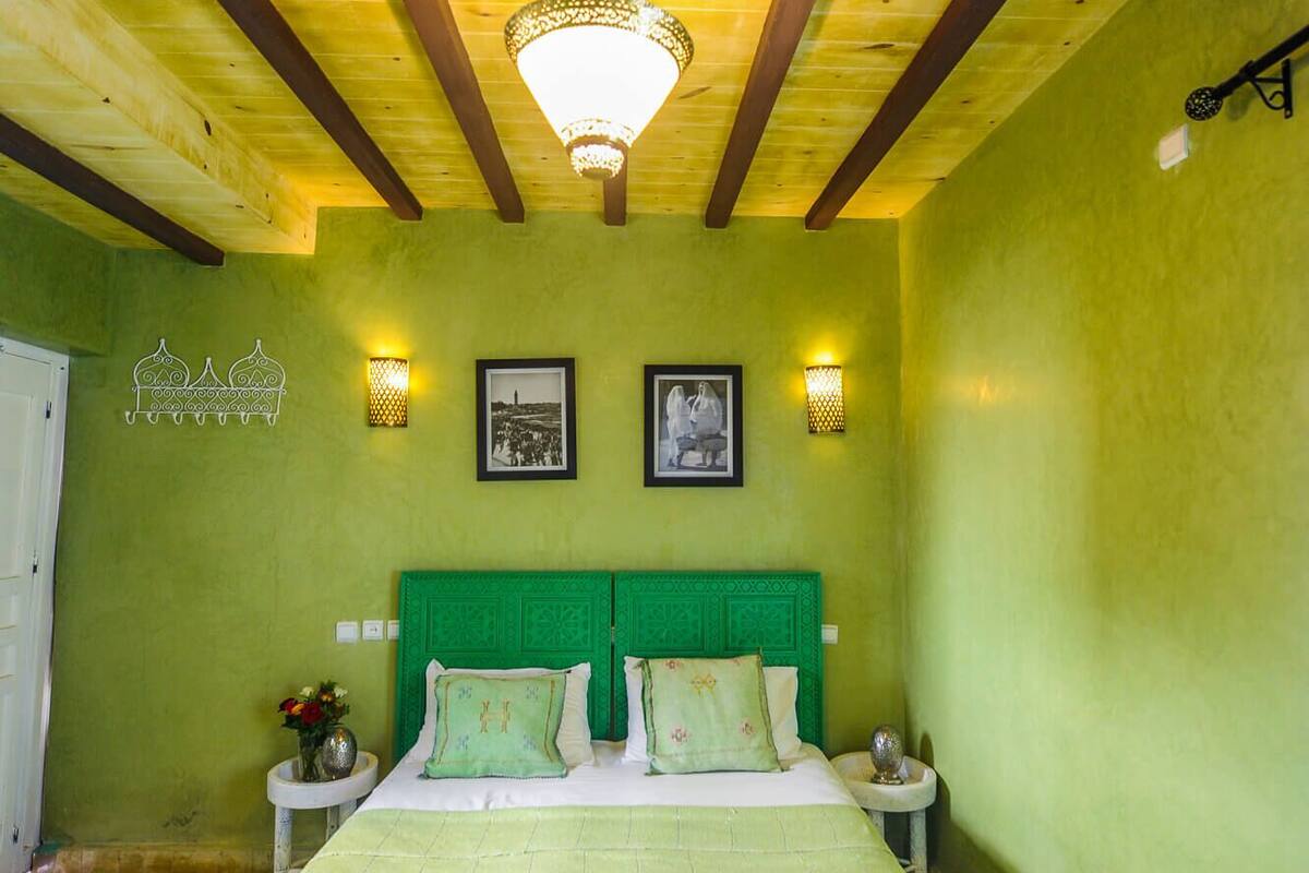 A room with a bed, two bedside tables, a hanging light fixture, and two wall-mounted lamps.