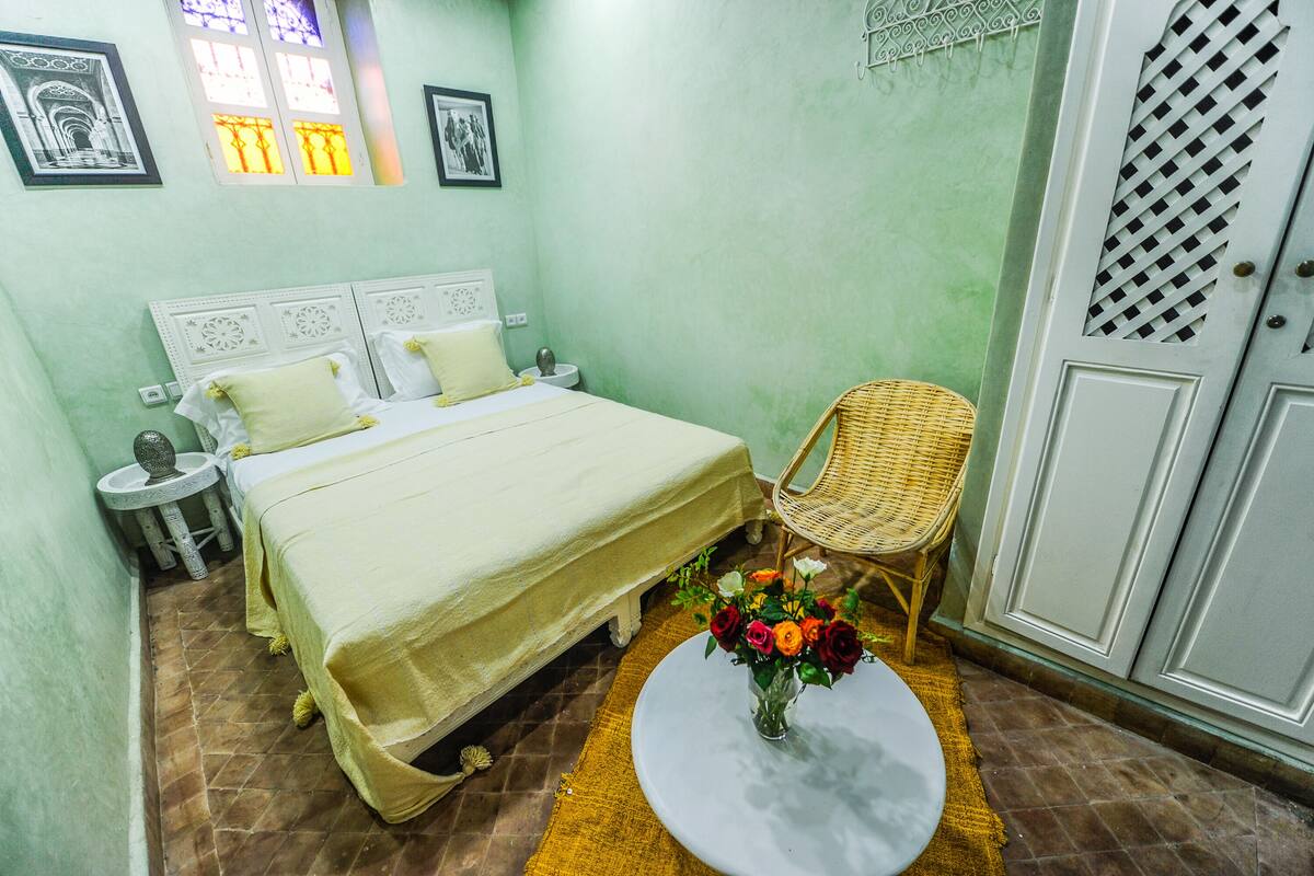 A bedroom with a bed, a chair, a small table with a vase of flowers, and a wardrobe.