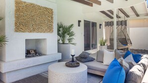 Un espace extérieur moderne, aménagé avec un foyer en pierre, un fauteuil suspendu et un canapé agrémenté de coussins.
