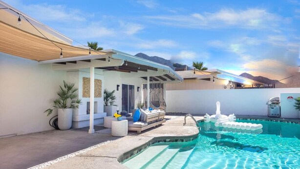 Un espace piscine extérieur moderne, doté d’un coin salon abrité, d’une piscine à l’eau d’un bleu cristallin et d’une vue sur les montagnes en arrière-plan.