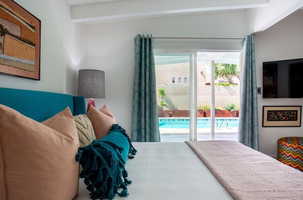 Habitación de hotel con cama, televisión, lámpara y vista a una piscina.