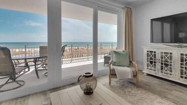 Un balcon avec vue sur la plage et l’océan, un coin salon avec une chaise et une table, et un téléviseur fixé au mur.
