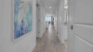 Un couloir aux murs blancs et au plancher en bois, qui mène à une pièce offrant une vue sur la mer.