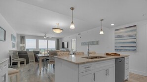 Une cuisine spacieuse dotée d’un grand îlot central, de luminaires suspendus et offrant une vue sur l’océan.