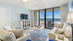 A living room with a television, a ceiling fan, a large window with a view of the beach, and a balcony with outdoor furniture. - Beachfront Seaside 5516, 2/2 Sea South Properties (Orange Beach)
