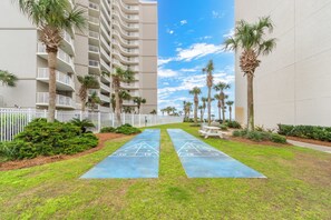 Un patio con una cancha de shuffleboard, palmeras y una cerca blanca.