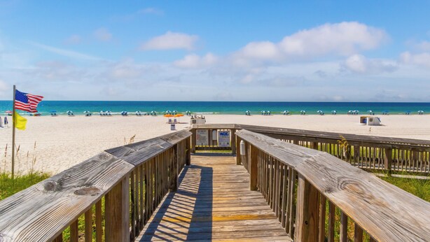 A wooden boardwalk leading to a beach with a flag, clear sky, and ocean view. - Beachfront Seaside 5516, 2/2 Sea South Properties (Orange Beach)