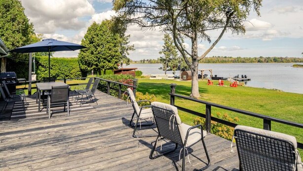 Een houten terras met tuinmeubilair, een barbecue en uitzicht op een meer met boten.