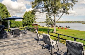 Eine Holzterrasse mit Gartenmöbeln, einem Grill und Blick auf einen See mit Booten.
