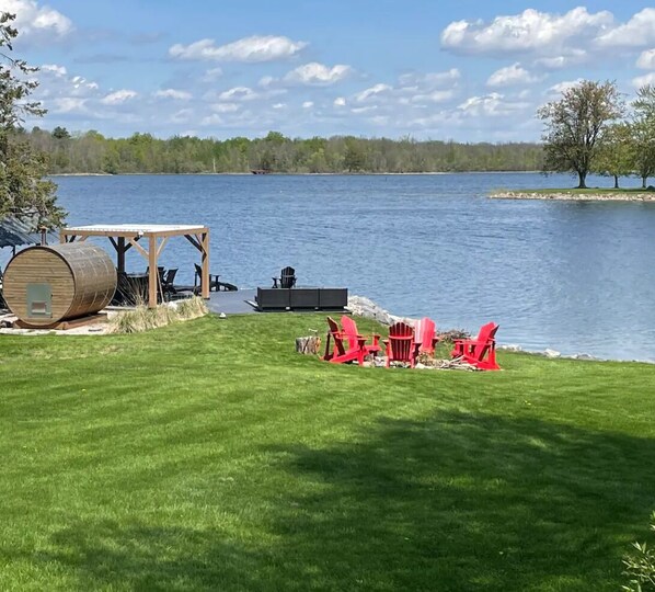 Eine Uferterrasse mit Holzdeck, roten Adirondack-Stühlen und einem Fass.