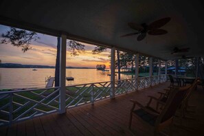 A covered deck with a view of a lake at sunset, wooden furniture, and a railing. - Sunset Cottage on Lake Wateree with Dock AND Ramp in a COVE (Camden)