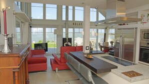 Una cucina moderna con una grande isola, sedute rosse e vista sul mare.