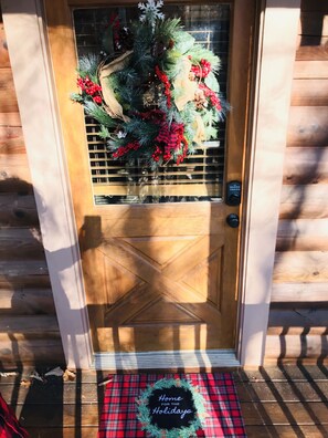 Welcome to a cozy holiday haven with a beautifully adorned entrance featuring a festive wreath and a warm doormat.