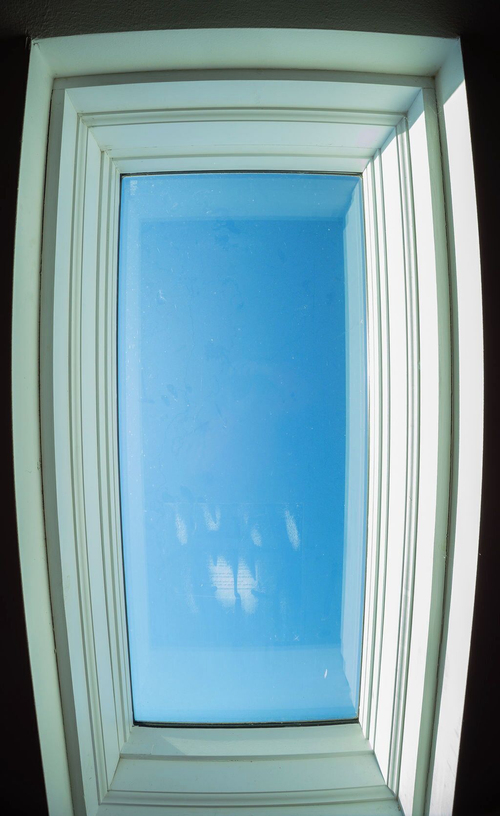 A square window with a clear blue sky view, framed by white and green trim.