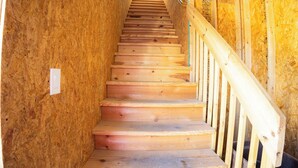 Een houten trap met een leuning, omgeven door onafgewerkte houten wanden.