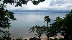 Une vue sur une plage, avec un ciel dégagé, une chaîne de montagnes lointaine et un petit bateau sur l’eau.