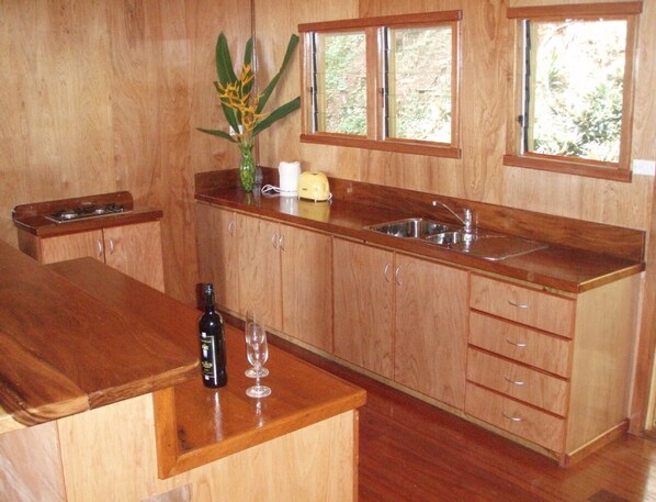 A kitchen with wooden cabinets, a countertop, a sink, a window, and a vase with flowers. - Beach Lodge with Spectacular Ocean Views (Savusavu)