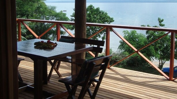 Une terrasse en bois avec une table et des chaises, offrant une vue sur une étendue d’eau et des montagnes lointaines.