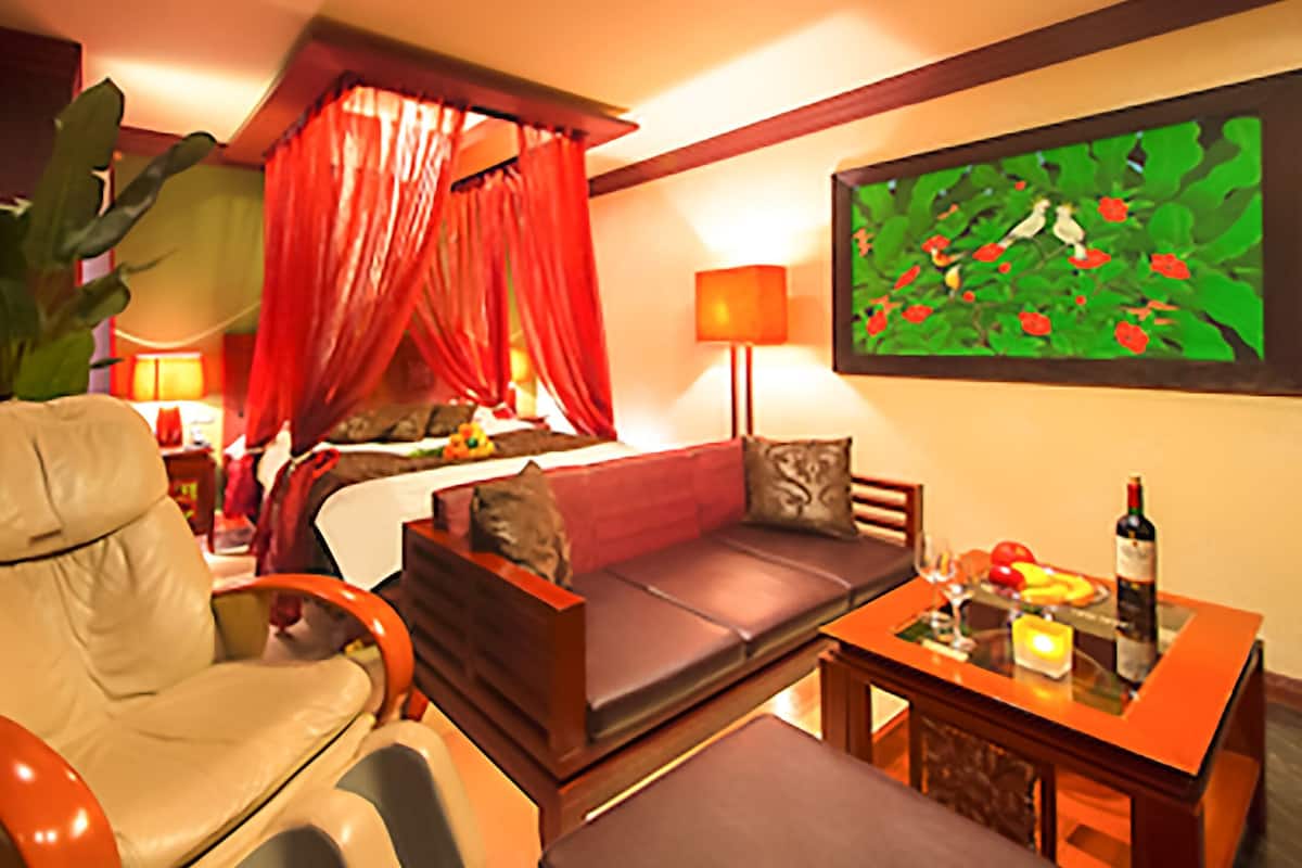 A hotel room with a bed, a sofa, a chair, a table with a bottle, and a painting on the wall.