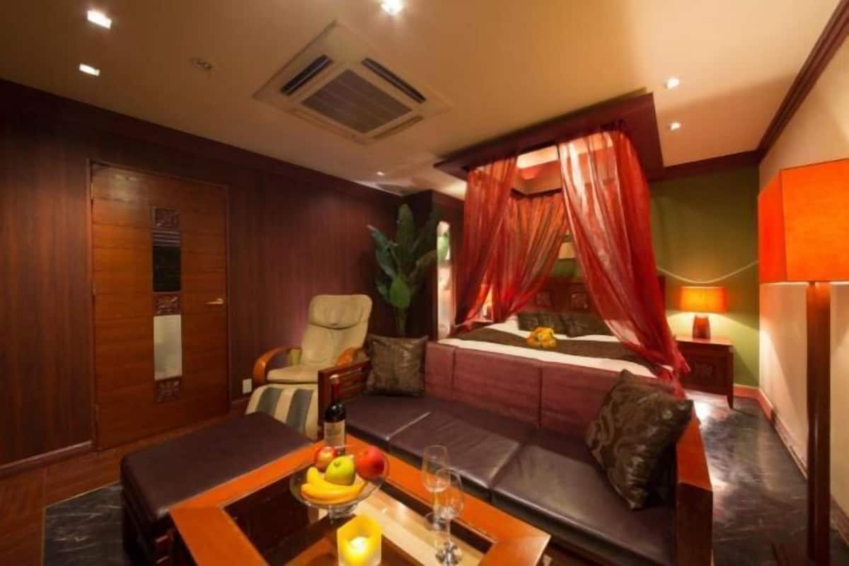 A bedroom with a bed, a sofa, a table with fruits and a candle, and a nightstand with a lamp.
