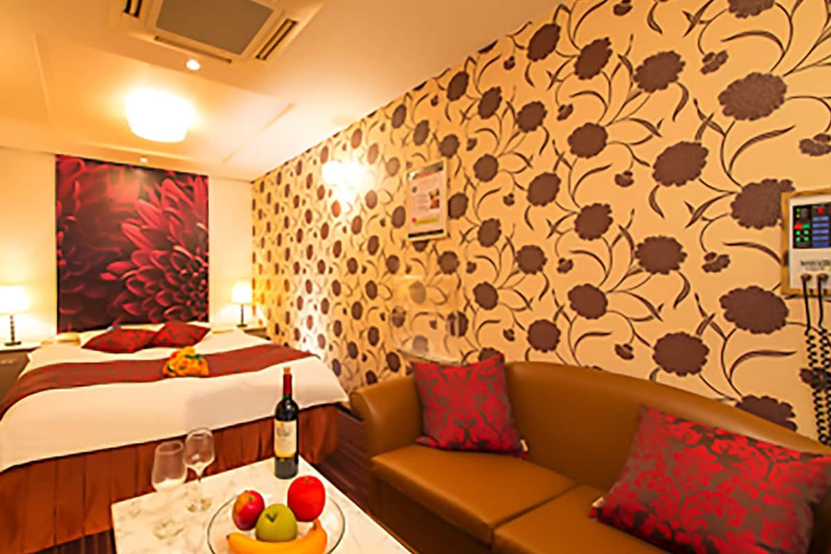 A hotel room with a bed, a sofa, a table with a bottle, glasses, and fruit.