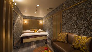 A hotel room with a bed, a sofa, a fruit bowl, and a bottle of wine.