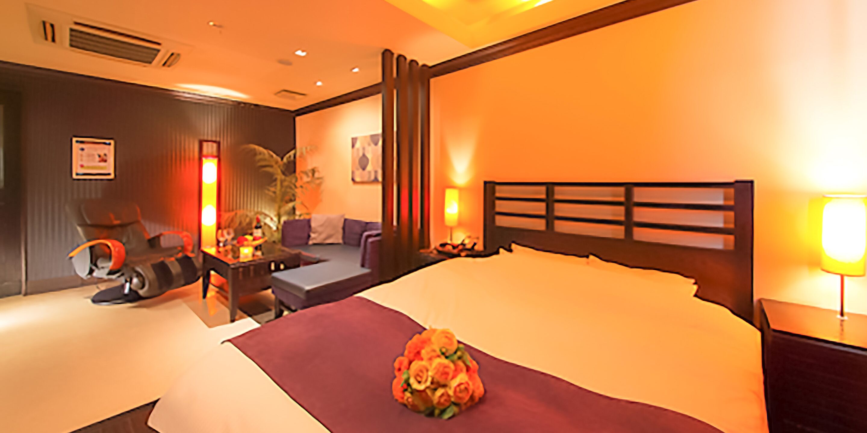 A hotel room with a large bed, a desk with a chair, a sofa, and a small table with a lamp.