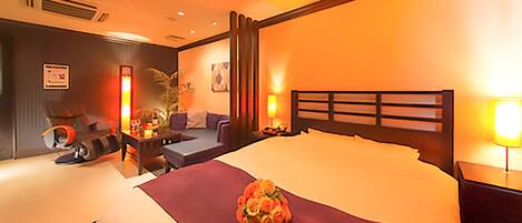 A hotel room with a large bed, a desk with a chair, a sofa, and a small table with a lamp.
