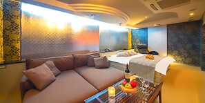 A modern hotel room with a large sofa, a bed, a dining table with fruit and wine, and a view of the city. - HOTEL Gt Kansai International Airport - Adults Only (Tajiri)