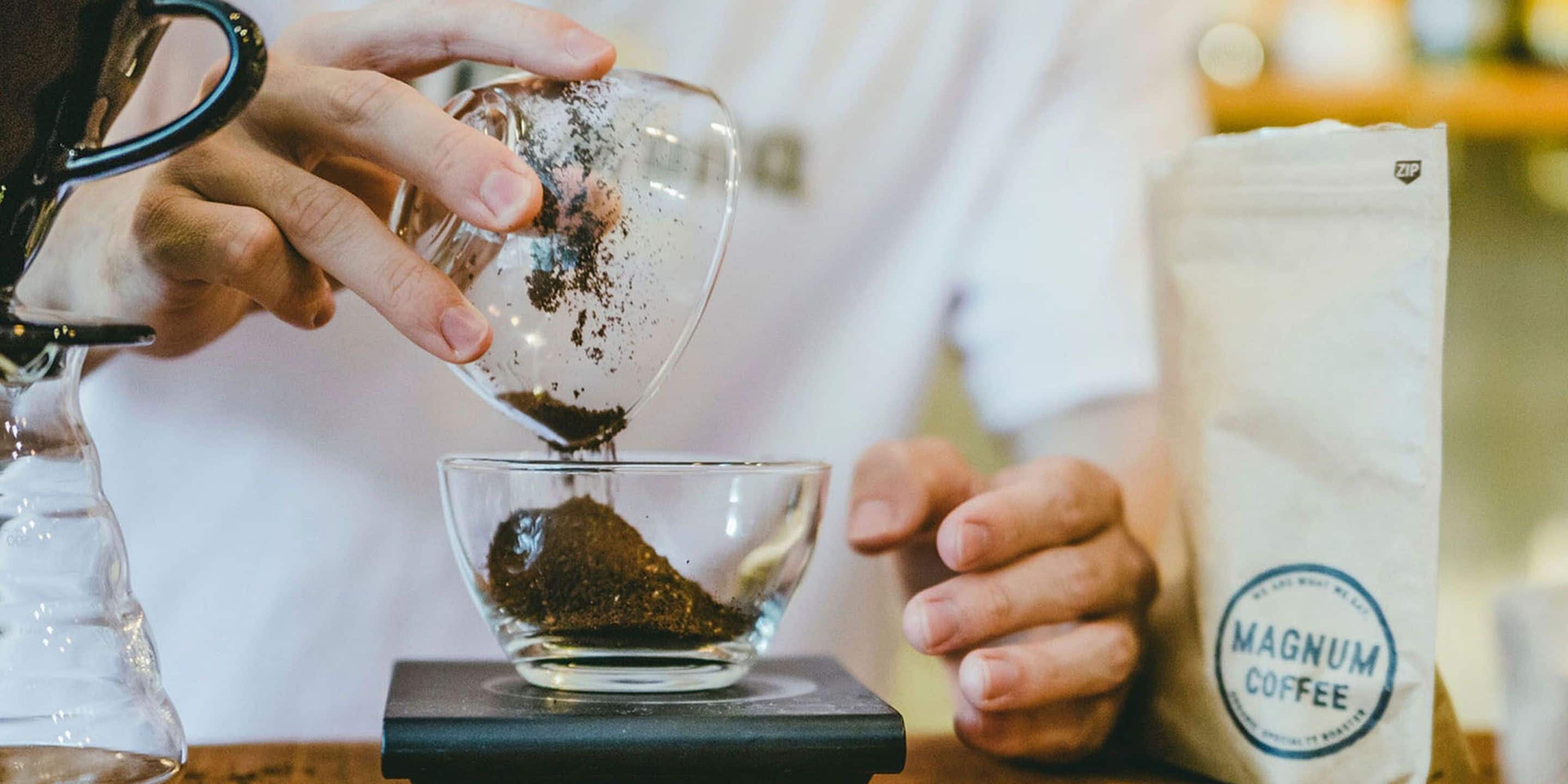 A person pouring coffee grounds into a glass cup.