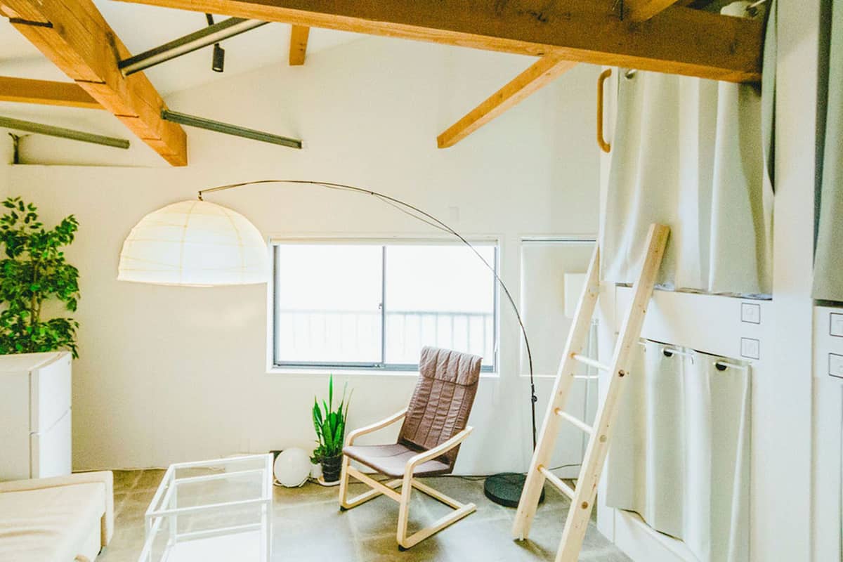 A modern living room with a white sofa, a rocking chair, a floor lamp, and a large window.