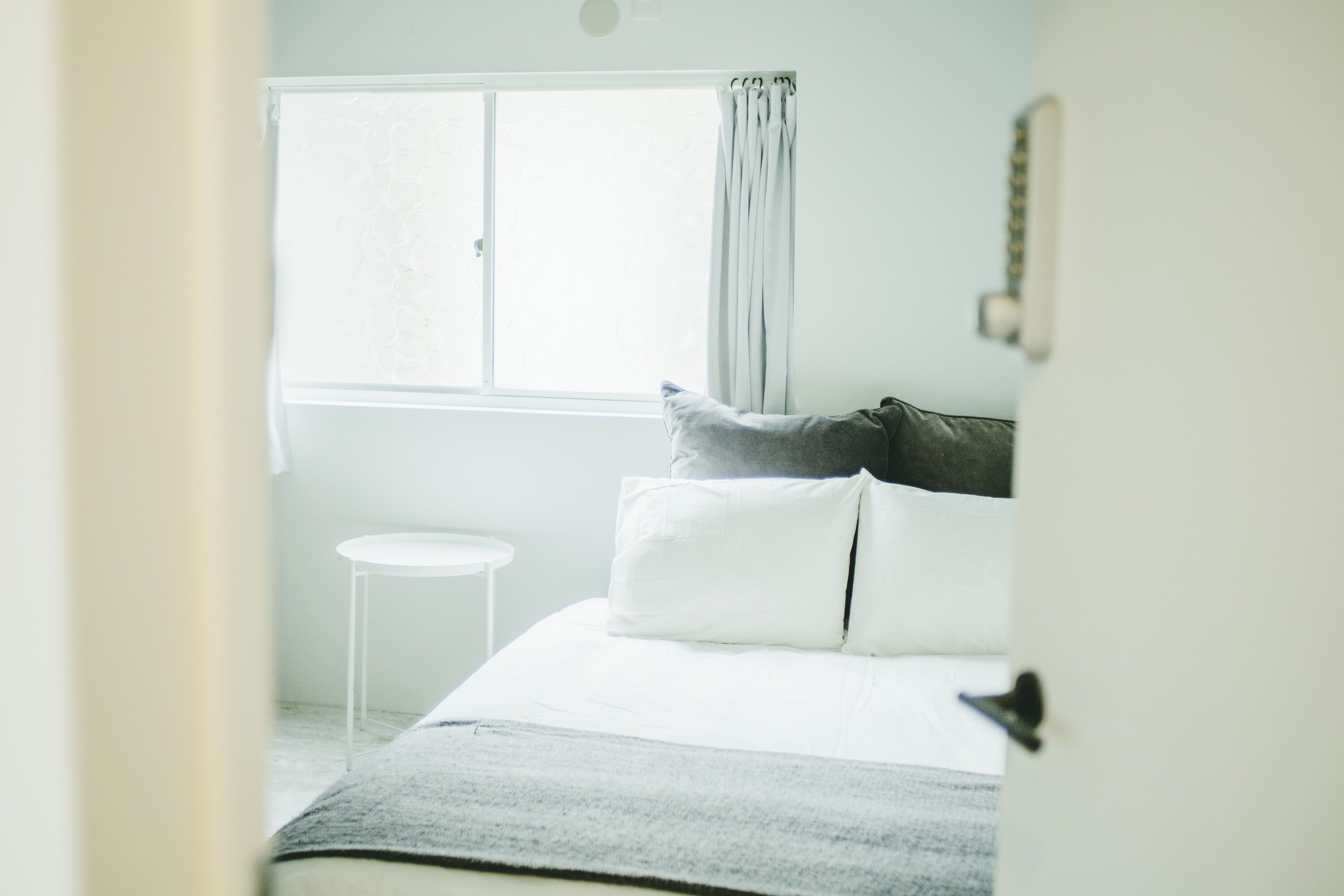 A bedroom with a bed, a window with curtains, a bedside table, and a wall-mounted light fixture.