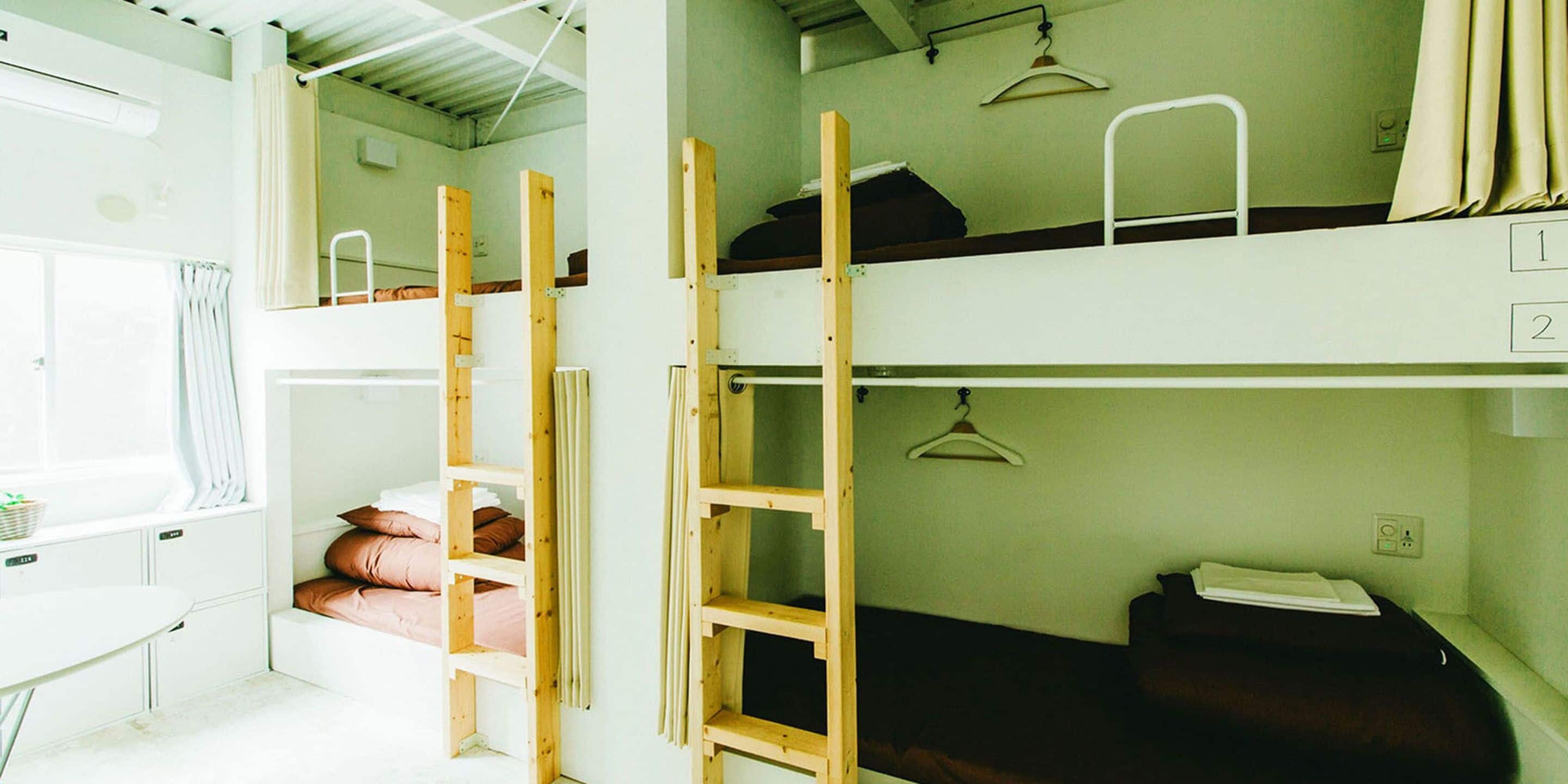 A dormitory room with bunk beds, a desk, and a window with curtains.