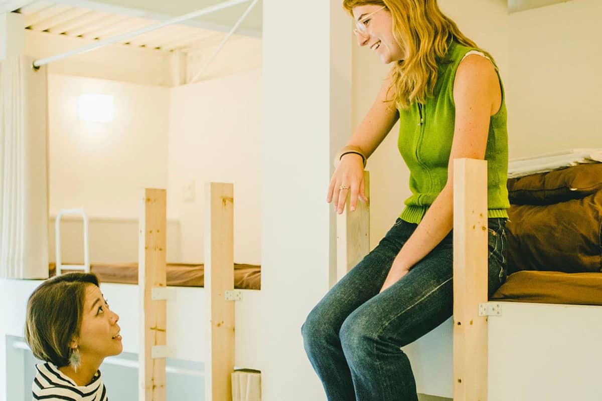 A dormitory room with bunk beds, a ladder, and a bed with a blanket.