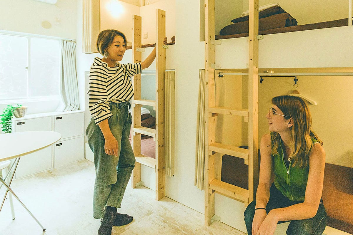 A room with bunk beds, a small table with a plant, and a couch with a pillow.