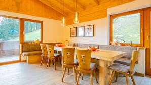 Un espace repas avec une table et des chaises en bois, de grandes fenêtres et une vue sur l’extérieur.