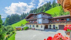Un chalet à deux étages doté de balcons, entouré d’une végétation luxuriante et surplombant un ciel dégagé.