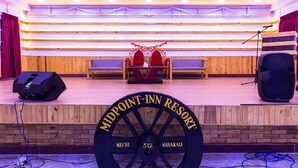 A stage with a podium, two red chairs, and a large wheel labeled "MIDPOINT- INN RESORT". - Midpoint Inn Resort (Ghankatta)