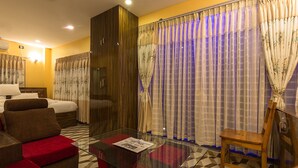A hotel room with a bed, a sofa, a glass coffee table, and a wooden chair. - Midpoint Inn Resort (Ghankatta)