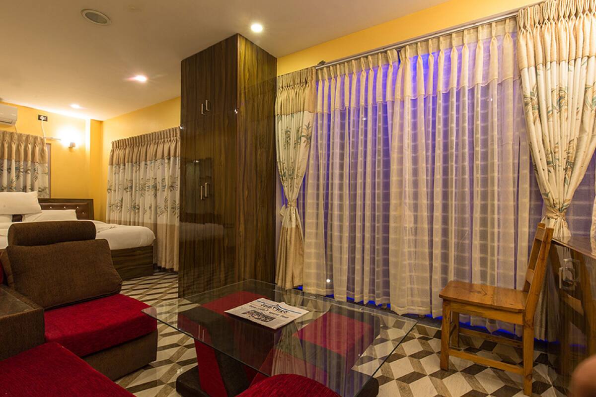 A hotel room with a bed, a sofa, a glass coffee table, and a wooden chair.