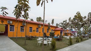 A courtyard with outdoor seating, a small fountain, and a building with a red roof and yellow walls. - Midpoint Inn Resort (Ghankatta)